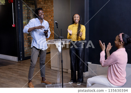 African American team celebrating successful presentation at podium in modern office 135630394