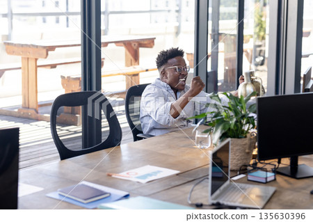 African American man celebrating success at office desk with joyful expression African American man celebrating success at office desk with joyful expression 135630396