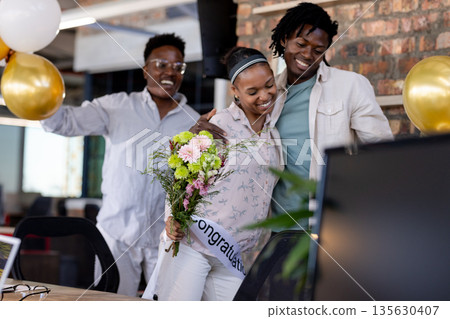 Congratulating coworker with flowers, African American colleagues celebrating success in office Congratulating coworker with flowers, African American colleagues celebrating success in office 135630407