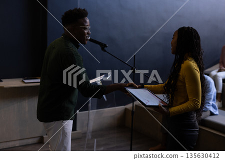 Man presenting award to woman on stage during business conference event Man presenting award to woman on stage during business conference event 135630412