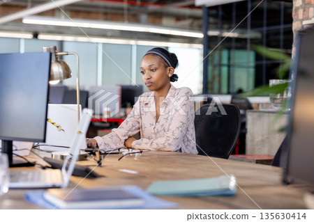 African American woman working on laptop in modern office, concentrating on task African American woman working on laptop in modern office, concentrating on task 135630414