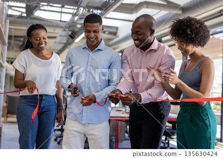 Diverse team celebrating office opening, cutting ribbon and smiling together 135630424