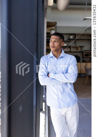 Businessman in light blue shirt standing by office window, looking thoughtful Businessman in light blue shirt standing by office window, looking thoughtful 135630432