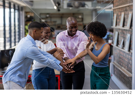 Diverse team in office celebrating success with hands together, smiling joyfully 135630452