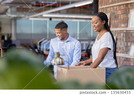 Colleagues unpacking boxes in modern office, smiling and collaborating on project Colleagues unpacking boxes in modern office, smiling and collaborating on project 135630455