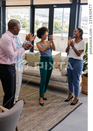 Colleagues applauding and celebrating success in modern office with large windows 135630477