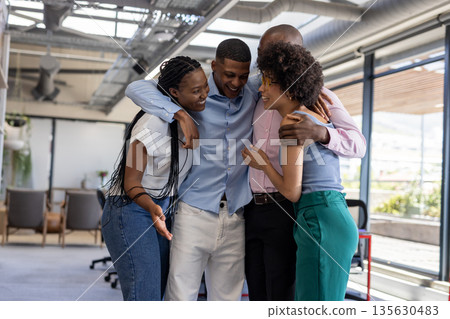 Diverse colleagues in office hugging and laughing, celebrating team success together Diverse colleagues in office hugging and laughing, celebrating team success together 135630483