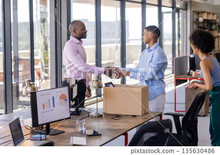 Colleagues shaking hands in modern office, welcoming new team member with box Colleagues shaking hands in modern office, welcoming new team member with box 135630486