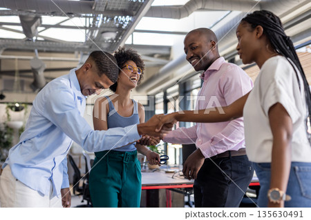In office, colleagues shaking hands, smiling, celebrating successful teamwork together In office, colleagues shaking hands, smiling, celebrating successful teamwork together 135630491