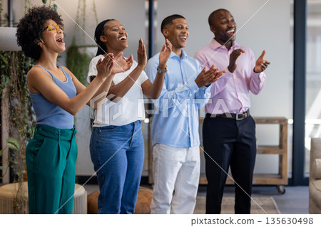 Diverse group of professionals clapping and smiling in modern office setting 135630498