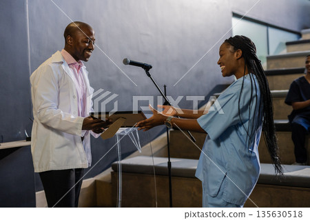 African American woman in scrubs receiving award from smiling man in white coat African American woman in scrubs receiving award from smiling man in white coat 135630518
