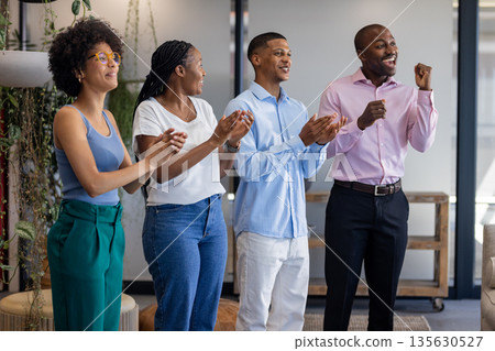 Diverse team celebrating success in office, clapping and smiling with excitement 135630527