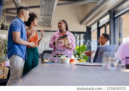 Colleagues celebrating farewell with cake and gifts in modern office setting 135630555