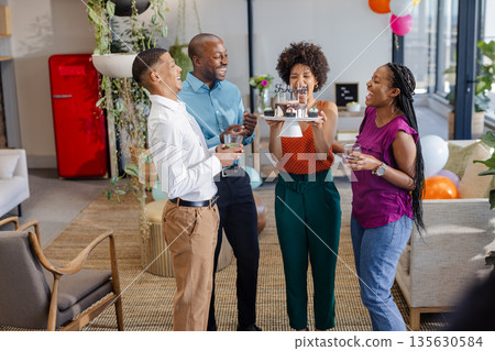 Holding drinks and laughing, African American colleagues celebrating birthday in office 135630584