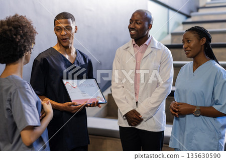 Discussing award certificate, medical professionals smiling and engaged in hospital hallway 135630590