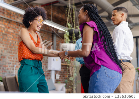 Colleagues in office laughing and shaking hands, enjoying team bonding moment 135630605