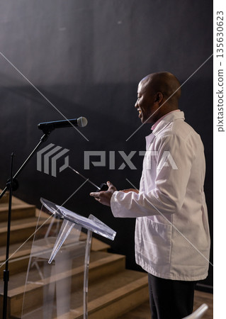 African American man presenting with microphone at podium in conference hall African American man presenting with microphone at podium in conference hall 135630623