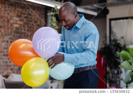 Businessman in blue shirt arranging colorful balloons at office celebration event Businessman in blue shirt arranging colorful balloons at office celebration event 135630632