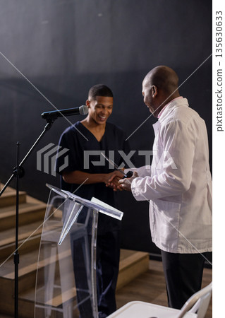 Man receiving award on stage, smiling and shaking hands with presenter 135630633