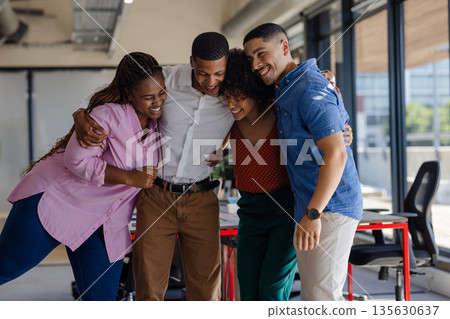 Diverse colleagues embracing and laughing together in modern office setting Diverse colleagues embracing and laughing together in modern office setting 135630637