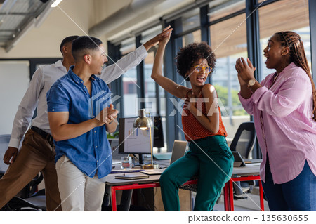 Colleagues celebrating success with high fives in modern office setting Colleagues celebrating success with high fives in modern office setting 135630655