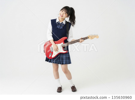 錄音室裡,一名身穿制服的高中女生抱著一把紅色電吉他,歪著頭微笑。 錄音室裡,一名身穿制服的高中女生抱著一把紅色電吉他,歪著頭微笑。 135630960