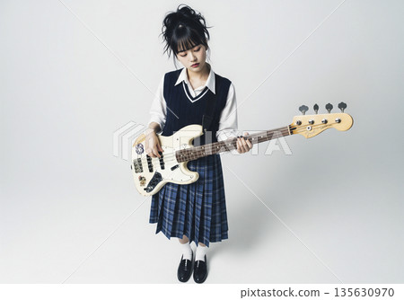 A female bassist holding a bass guitar and showing a cute, slightly shy smile in front of a yellow background 135630970