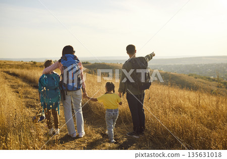 Family hikers with backpacks exploring nature trail at sunset in golden grassland 135631018