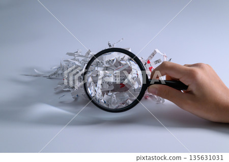 Hand examining shredded paper with a magnifying glass 135631031