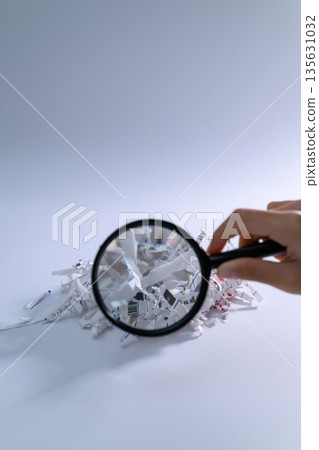 A hand examining shredder debris with a magnifying glass 135631032