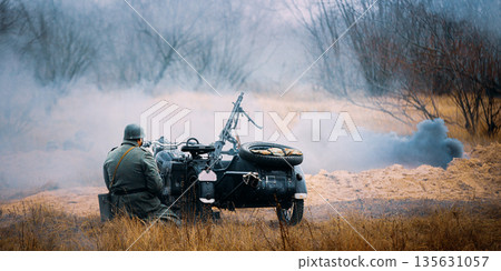 Re-enactor Dressed As World War Ii German Wehrmacht Infantry Soldier Sit Near Old Tricar, Armed Machinegun. Smokescreen. Army Three-wheeled Motorcycle In Autumn Field. Battlefield 135631057