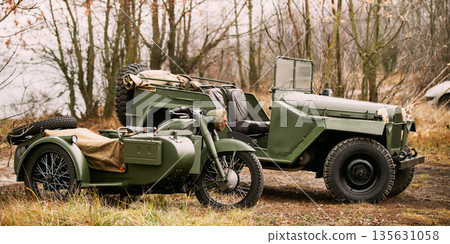 Old Tricar, Three-Wheeled Gray Motorcycle With A Sidecar Of German Forces and Willys Mb (jeep, U.s. Army Truck, 4x4) Parked At Forest During Reconstruction Of Some Fight World War II 135631058