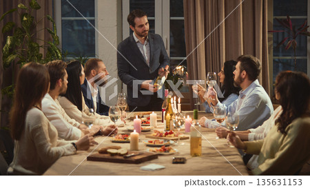 Man presenting wine bottle to friends at dinner table. Man presenting wine bottle to friends at dinner table. 135631153