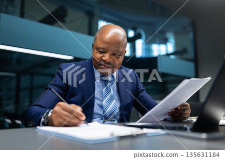 Confident African American businessman reviewing documents and signing paperwork at office desk 135631184