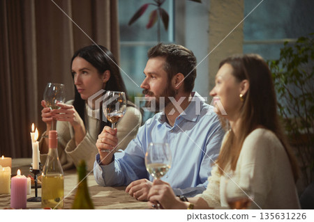 Friends in their thirties drinking wine at dinner table in cozy home interior. Friends in their thirties drinking wine at dinner table in cozy home interior. 135631226
