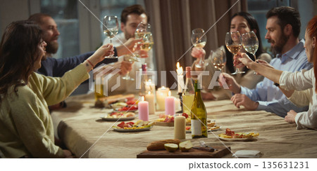Friends talking over wine sitting around table in cozy home interior. 135631231
