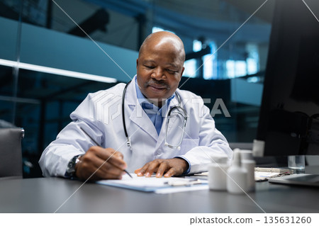 Black mature doctor writing medical notes at office desk, documenting paperwork Black mature doctor writing medical notes at office desk, documenting paperwork 135631260