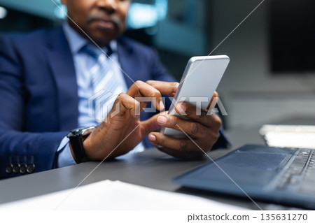 Closeup of African American businessman using smartphone at his desk Closeup of African American businessman using smartphone at his desk 135631270