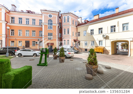 Urban courtyard with historic architecture, cars, and green topiary 135631284