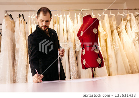Male tailor or seamstress taking mannequin measurements for cloth pattern with measuring tape in fashion design studio, woman designer working with dummy in workshop, dressmaking and sewing concept Male tailor or seamstress taking mannequin measurements for cloth pattern with measuring tape in fashion design studio, woman designer working with dummy in workshop, dressmaking and sewing concept 135631438