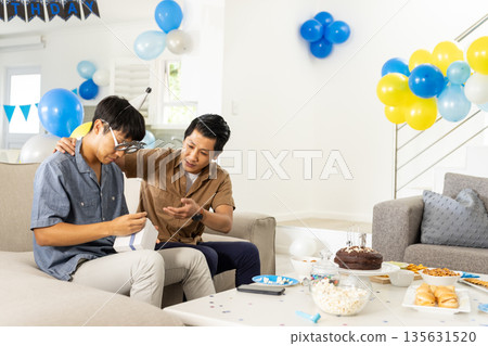 Father and son celebrating birthday at home, opening gifts with joy 135631520