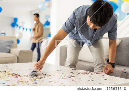Man cleaning confetti from table at home after festive celebration 135631548