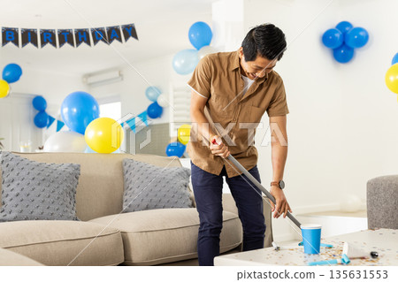 Smiling man cleaning living room after birthday party, surrounded by balloons Smiling man cleaning living room after birthday party, surrounded by balloons 135631553