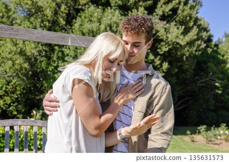 Couple embracing outdoors, woman showing engagement ring, both smiling joyfully 135631573