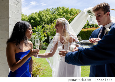 Bride in veil sharing champagne with guests at outdoor wedding celebration 135631577