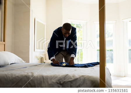 Groom preparing suit on bed in bright room, smiling with excitement 135631581