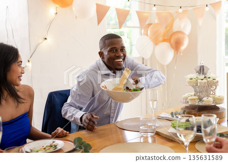 Serving salad at wedding celebration, joyful man surrounded by friends and decorations Serving salad at wedding celebration, joyful man surrounded by friends and decorations 135631589