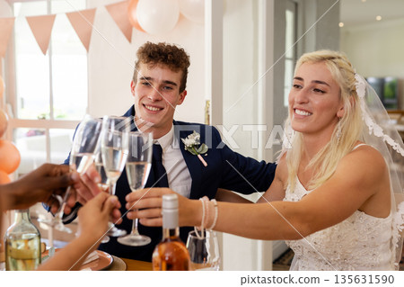 Bride and groom toasting with friends, celebrating joyful wedding reception indoors 135631590