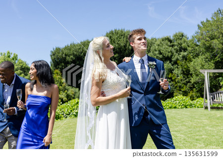 Celebrating outdoors, bride and groom holding champagne glasses with smiling friends 135631599