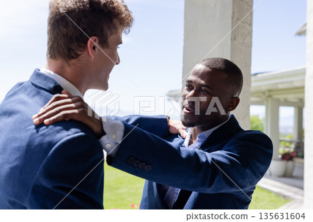 Groom and friend in blue suits sharing joyful moment at wedding celebration 135631604